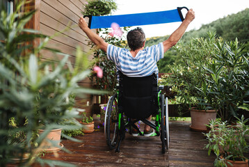 Rear view of senior man in wheelchair doing exercise on terrace.