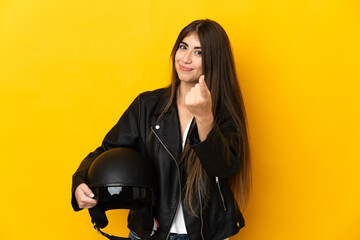 Young caucasian woman holding a motorcycle helmet isolated on yellow background doing coming gesture