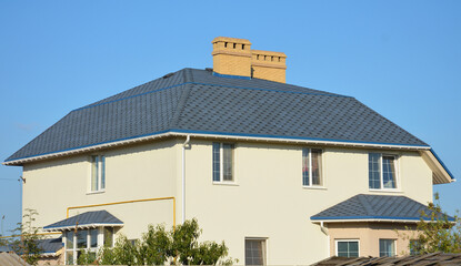 Facade of a large mansion, house with an asphalt shingled roof with a flashing around brick chimneys, roof gutters, gas pipe, air conditioner on a painted stucco exterior walls that need renovation.