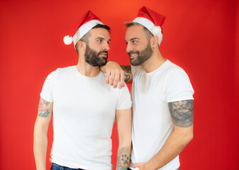 Obraz premium Happy gay couple in santa hat and casual clothes over red background.