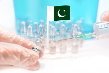 Hands holding a vaccine vial and a syringe with rows of the same capsules and a flag of Pakistan in the background, illustrating plans for global vaccination against Covid-19 (SARS-CoV-2).