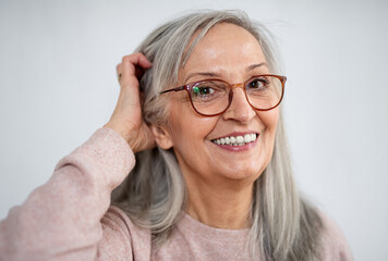 Portrait of senior woman standing indoors against light background, looking at camera.