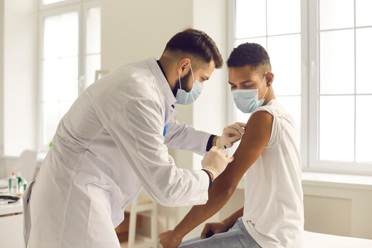 Doctor in face mask giving antiviral vaccine to young patient during vaccination campaign - Powered by Adobe