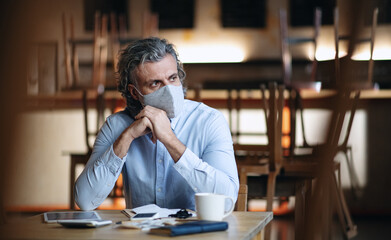 Frustrated owner sitting at table in closed cafe, small business lockdown due to coronavirus.