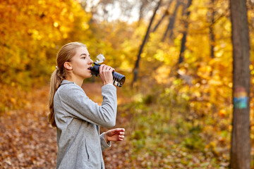 woman drinking water from a bottle, caucasian female refresh her body after running workout at sunny autumn day. running makes your body stronger