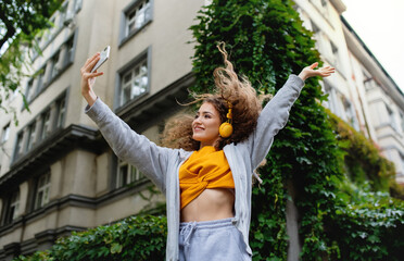 Young woman with smartphone dancing outdoors on street, tik tok concept. - obrazy, fototapety, plakaty