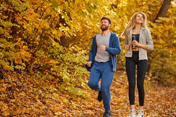 married couple run together in the autumn forest, athletic sportive man and woman in sportswear enjoy jogging on fresh air, at sunny day