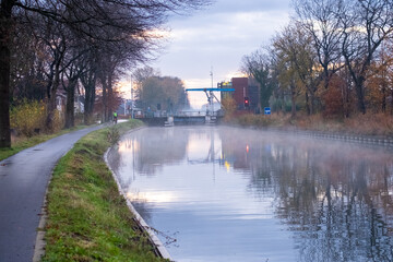 River stream canal bending with grass banks and wild flowers and trees in a scenic landscape on a misty autumns morning sunrise day. High quality photo
