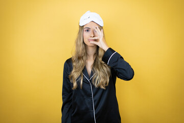 Young pretty woman wearing sleep mask and pajamas over isolated yellow background WITH mouth and...