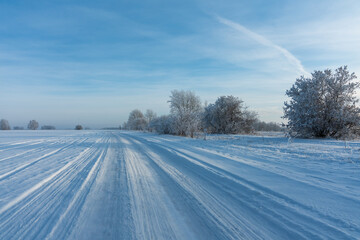 Fototapeta premium Snow covered winter field with trees and road going through to the horizon. Winter landscape. Beautiful winter nature.