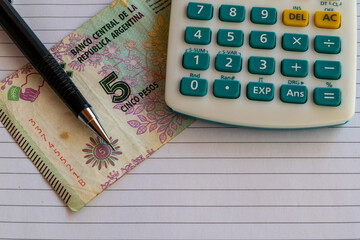 calculator, five argentine pesos banknotes on sheet of paper with mechanical pencil