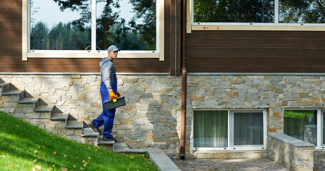 Full length shot of young workman in blue overalls carrying toolbox after doing repair work in the house