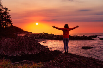 Fototapeta premium Wild Pacifc Trail, Ucluelet, Vancouver Island, BC, Canada. Adventurous Girl Enjoying the Beautiful View of the Rocky Ocean Coast. Colorful Sunset Sky. Concept: Travel, adventure, freedom