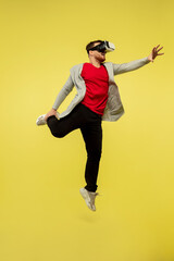 Playing VR-headset. Full length portrait of young high jumping man gesturing isolated on yellow studio background. Attractive male caucasian model. Copyspace. Human emotions, facial expression concept