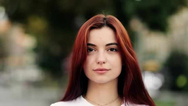Cute woman with red hair walking on the street look at camera. Portrait of Beautiful Young Woman with Red Hair Looking Up to the Camera and Smiling Charmingly