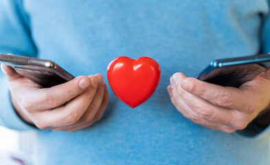 Big flying red heart. Mobile phones, smartphones in hands. Valentine's day holiday concept. Online love, remote communication on internet, social networks.Virtual dating,calls, technology.Coronavirus