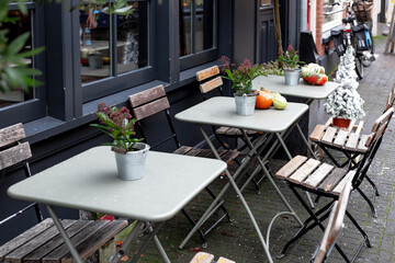 Street cafe during Christmas with pumpkins and Red Skimmia flowers European style. Outdoor tables with chairs on cafe terrace in Amsterdam. Vintage Europe, New Years holidays in retro style outdoor