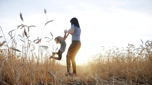 mom play with her daughter the park in wheat field. happy family people in the park concept. mom play is spinning daughter holding hands in wheat field. childhood dream happy fun family