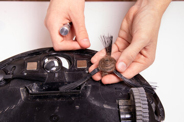 The master is holding a robot vacuum cleaner brush with hair wrapped around it, close-up.