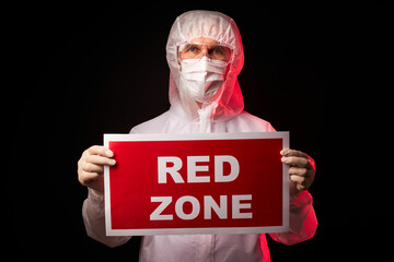 doctor male in protective medical suit holding tablet with RED ZONE inscription, warn people against danger, isolated on black background with red UV rays