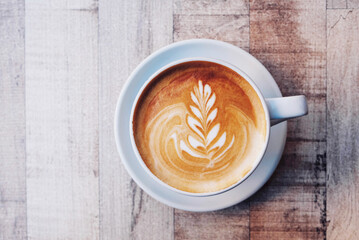 Cup of fresh delicious cappuccino coffee with beautiful latte art on wooden background, close up....