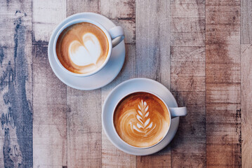 Two cups of fresh delicious cappuccino coffee with beautiful latte art on wooden background. From above, copy space.