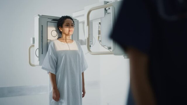 Hospital Radiology Room: Beautiful Latin Woman Standing while Female Radiologist Adjusts X-Ray Machine. Preventive Treatment Scanning Chest, Back, Breast, Lungs. Modern Clinic with Advanced Technology