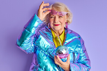 excited elderly woman celebrate the party, drink beverage alone posing at camera isolated over purple background. in stylish warm outfit