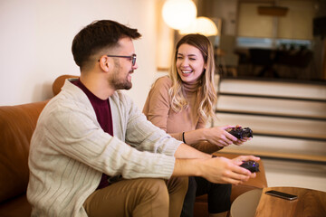 Young couple playing video games at home, sitting on sofa and enjoying themselves