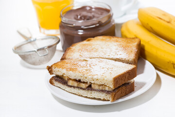 sweet sandwich with chocolate paste and banana for breakfast on white table