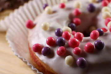 White icing donut with small colored pieces of chocolate on a wooden table against purple background