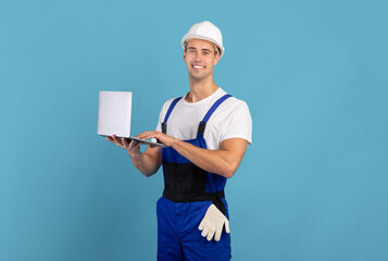 Man in coveralls and hard hat using laptop computer on blue background