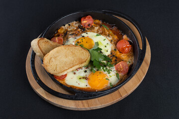 healthy breakfast shakshuka - fried eggs, onion, bell pepper, tomatoes and spices in cast iron stewpan on old wooden plank.