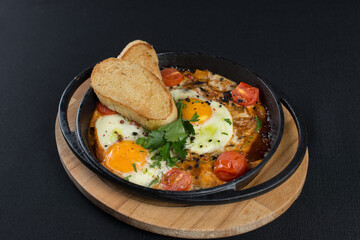 healthy breakfast shakshuka - fried eggs, onion, bell pepper, tomatoes and spices in cast iron stewpan on old wooden plank.
