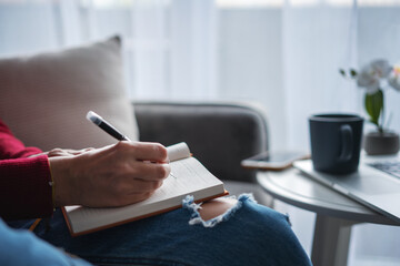 Female hands making notes in a notebook in front of laptop screen, online education and work concept