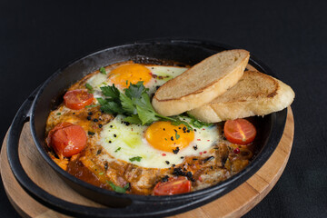 healthy breakfast shakshuka - fried eggs, onion, bell pepper, tomatoes and spices in cast iron stewpan on old wooden plank.
