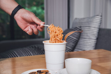 Hand of a man holding a plastic fork with cooked instant noodles. A cup of instant noodle with fork ready to eat convenient and delicious food.