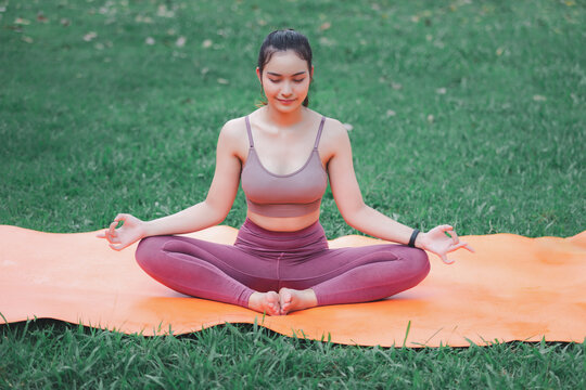 Asian woman practicing yoga in Root Bond, Mula Bandha pose on the mat in outdoor park.