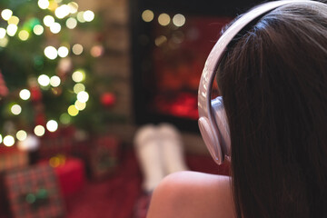 Woman in headphones sitting and warming at winter evening near fireplace flame and  christmas tree.