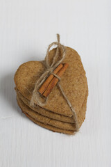 Heart-shaped gingerbread cookie tied with twine. It has a cinnamon stick on it. On boards painted white. Close-up shot.