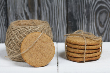 Gingerbread cookies tied with twine. Nearby is a cinnamon stick and a skein of string. On boards painted white. Close-up shot.