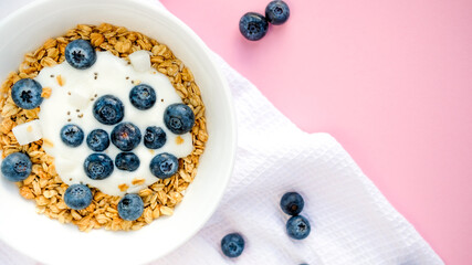 Delicious homemade muesli and blueberries served on a pink table with a white napkin, top view with space for text. Healthy breakfast