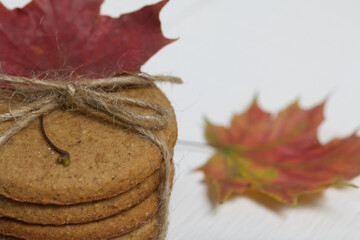 Gingerbread cookies tied with twine and autumn maple leaves. On boards painted white. Close-up shot.