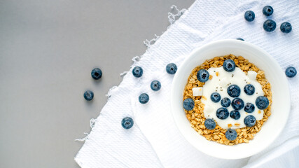 a bowl of handmade granola with blueberries added coconut and Chia seeds. located on a gray background with a white napkin. space for text . the view from the top