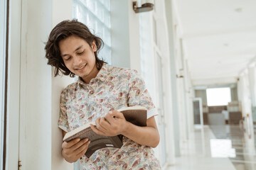 Portrait of happy male student reading holding book on campus.