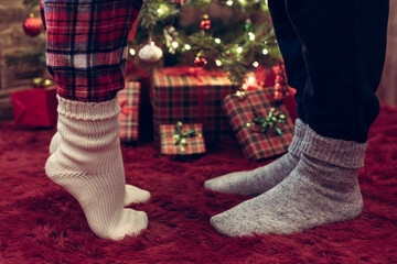 Woman feet standing in tip toe in winter socks near male lags on a fluffy red blanket near a...