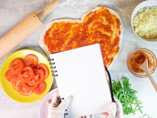 Hands holding empty note pad on pizza ingredient and basis on background