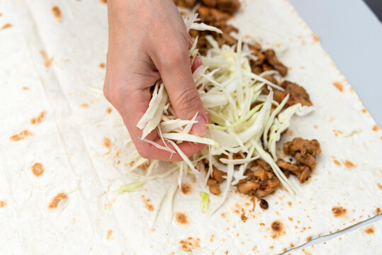 The girl pours chopped cabbage from her hand onto pita bread with meat.