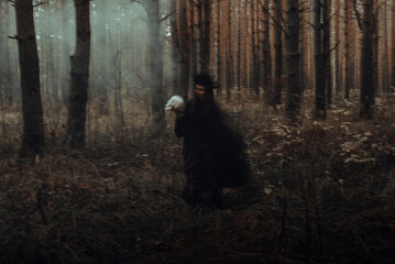 blurred silhouette of a terrible witch with a skull in her hands performing a mystical occult...