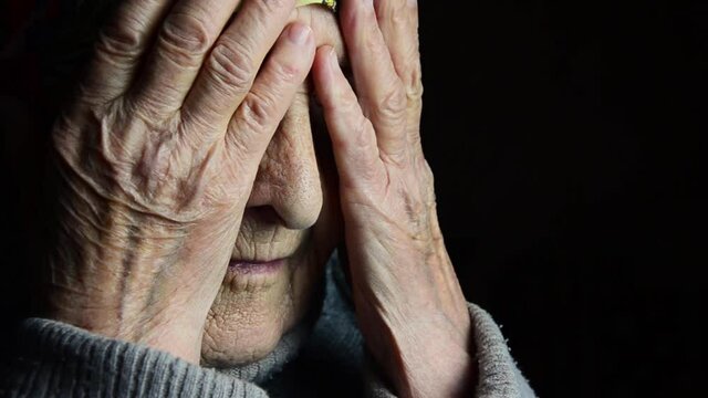Grandmother covers her face with her hands. Old grandmother's face close up. Old wrinkled hands of a grandmother on a dark background close-up. The wrinkles on the mother's arms. Child care concept 